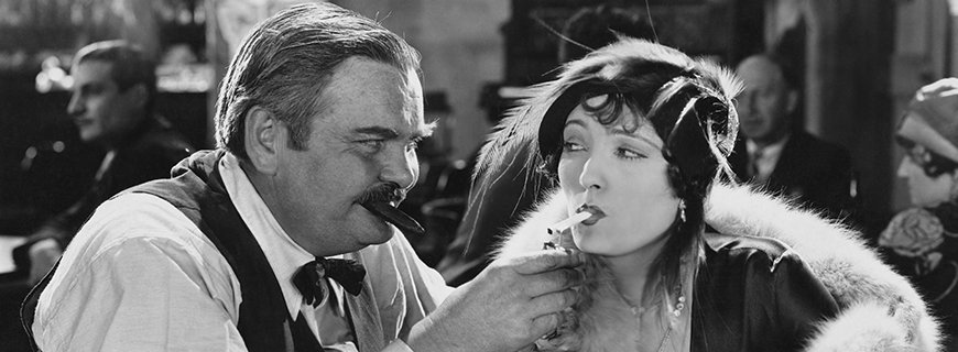ein Mann bietet einer Dame mit Zigarette im Mund Feuer an