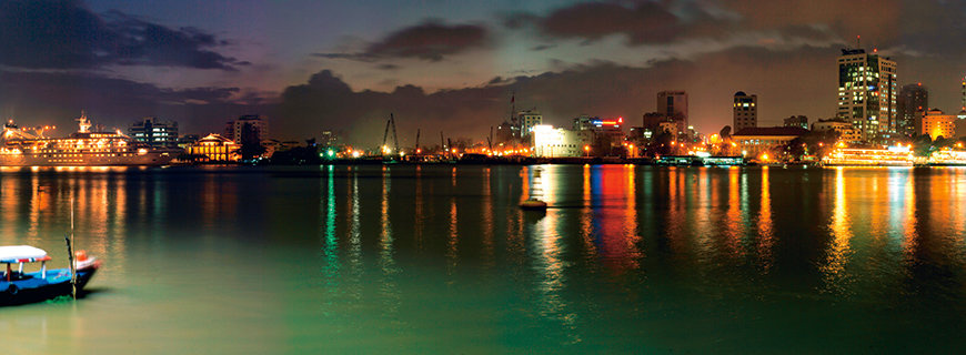 ein Hafen mit kleinen Booten, im Hintergrund das Leuchten der Stadt 