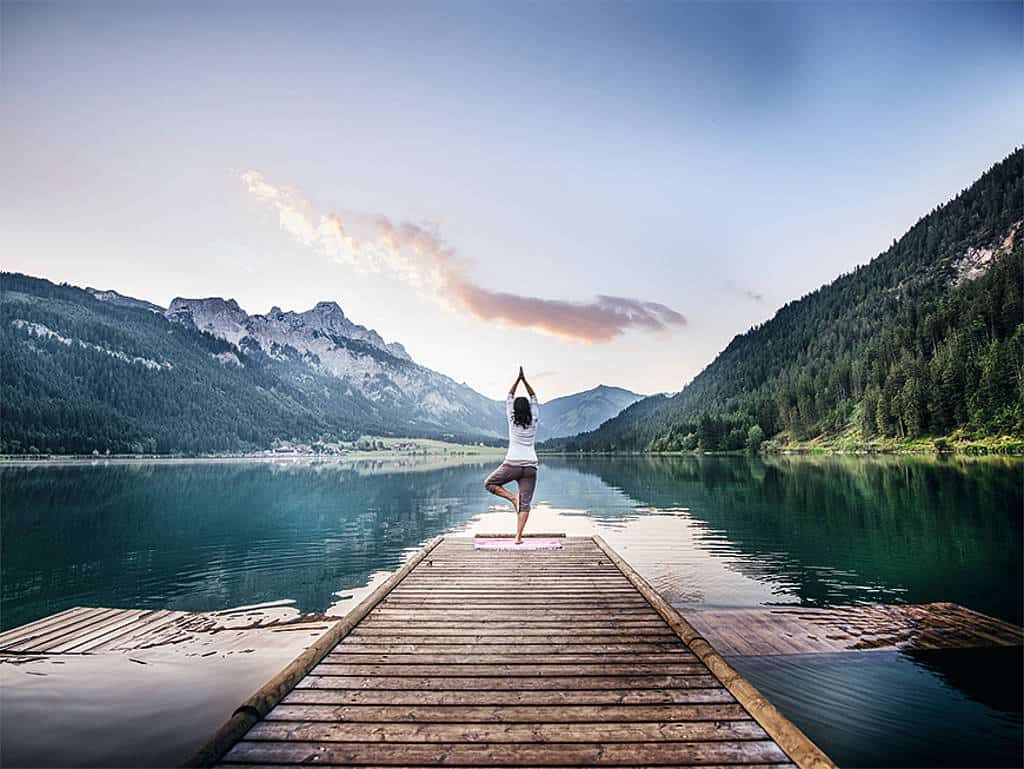 Eine Frau beim Yoga am Steeg eines Bergsees