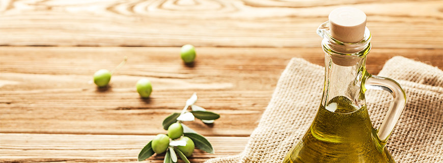 Olivenölflasche auf einem Tisch, mit einem Olivenölzweig daneben