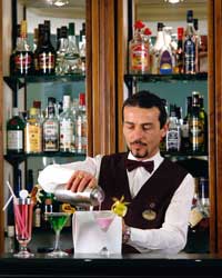 Ein Barkeeper steht hinter der Bar und mixt gerade einen Cocktail 