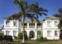 ein weißes Haus im Kolonialstil hinter zwei Palmen 