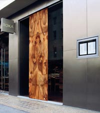 Das Logo und die Eingangstür des Restaurants Roka in London, eine Kombination aus großen Stahltüren und Holzverkleidungen 