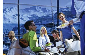 eine Gruppe junger Menschen genießt ihr Mittagessen auf einer Skihütte umschlossen von schneebedeckten Bergen 