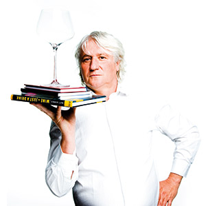 Reinhold Forobosko mit einem Glas Wein auf gestapelten Büchern