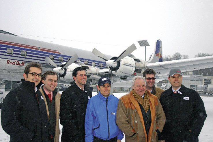 eine Gruppe von Männern stehen am Landeplatz vor einem Flugzeug und posieren für ein Foto 