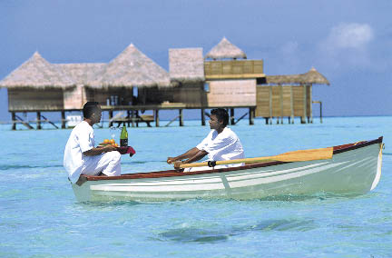 Zwei Einheimische auf einem Holzboot auf den Malediven mit einem Erfrischungsgetränk auf dem Weg zu den Gästen 
