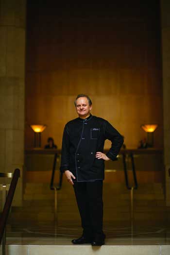 Joel Robuchon stehend in schwarzem Kochgewand mit der Hand in der Hüfte