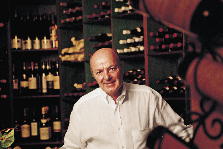 ein älterer Herr steht in einem Weinkeller vor einigen Regal befüllt mit diversen Flaschen 