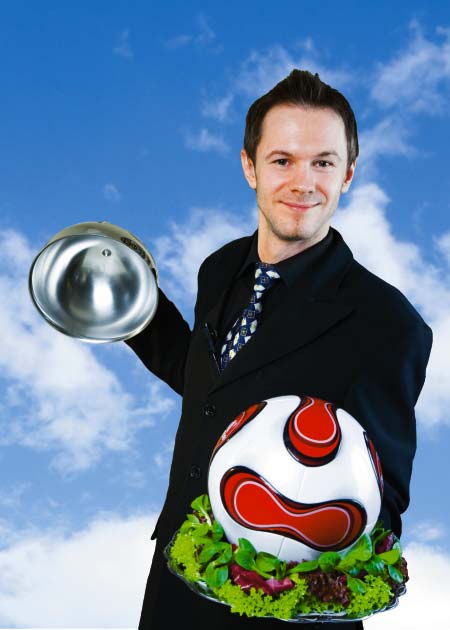 Ein Mann im Anzug öffnet die Cloche und darunter befindet sich ein Fußball auf Salat 