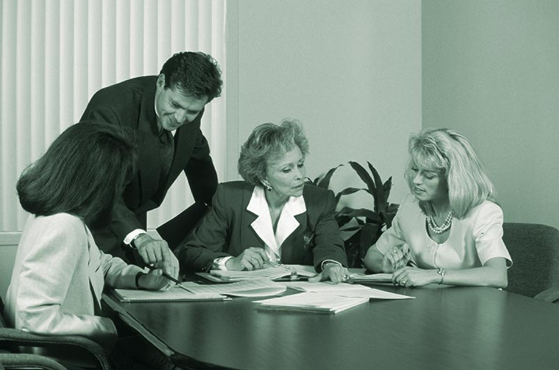 Ein Business Meeting in einem Konferenzraum bestehend aus einem stehenden Mann und drei sitzenden Frauen 