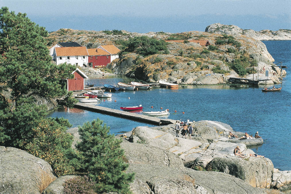 Norwegens Küste, ein langer Steg ins Wasser mit Holzbooten und Menschen beim Sonnenbaden 