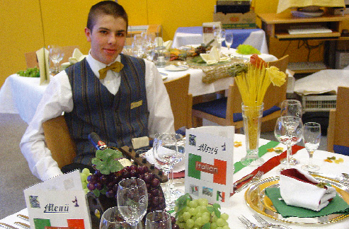 Ein junger Herr sitzt an einem Tisch vor ihm Weintrauben und Speisekarten 