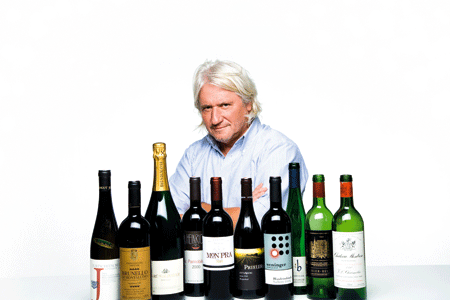 Ein Herr sitzt hinter einer Reihe von verschiedensten Flaschenweinen 