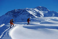 zwei Langläufer sind zu sehen, umgeben von reich an Schnee bedeckten Bergen 