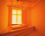 ein Bett vor einem Fenster in einem von orangenem Licht erfüllten Raum 
