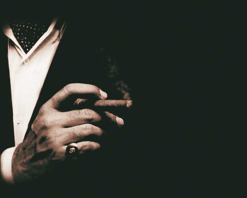 Mann mit Zigarre in der Hand in düsterer Atmosphäre