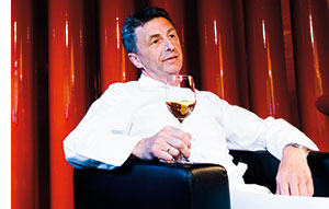 Hans Haas sitzt in einem roten Lederstuhl mit einem Glas Weisswein in der Hand