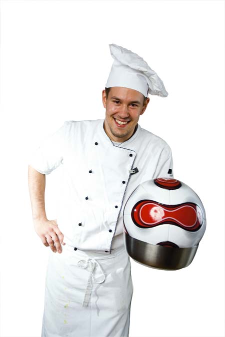 Ein junger Koch hält einen Kochtopf mit einem Fußball darin 