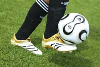 ein Fußball wird von einem Fußballspieler auf dem Rasen gekickt,man sieht nur die Füße bis zu den Knien 