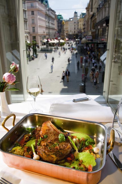 ein Rinderkotelette wird auf einem Tisch am Fenster serviert, während man den Bilck auf Wiens Graben genießen kann 