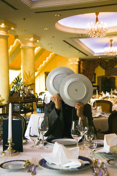 ein Herr sitzt in einem noblem Restaurant und versteckt sein Gesicht hinter zwei Tellern 