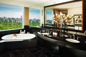 ein Einblick in ein Luxusbad, unter dem großen Fenster mit Blick auf den New Yorker Central Park steht eine Badewanne aus schwarzem Stein 