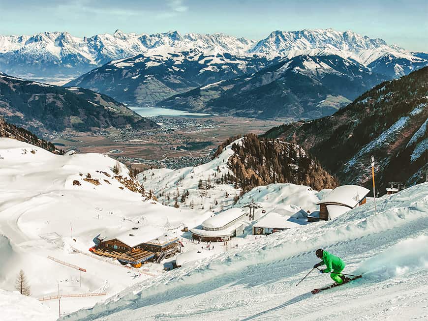 Ein Ski-Fahrer saust die Piste hinab, im Hintergrund schneebedeckte Gipfel
