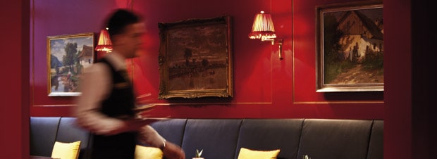 tiefrote Wände, blauer Pölstermöbel, der Kellner in Bewegung, ein Restaurant in Prag 